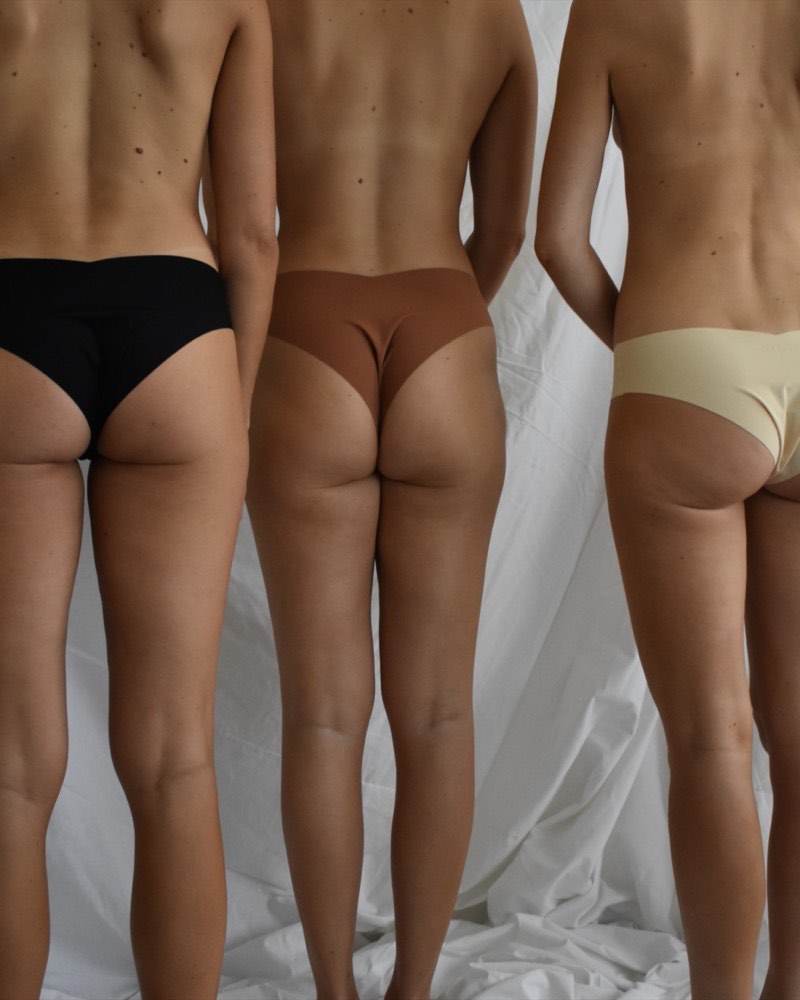 Three women photographed from behind after tanning, the colour even from shoulder to ankle across three different skin tones.